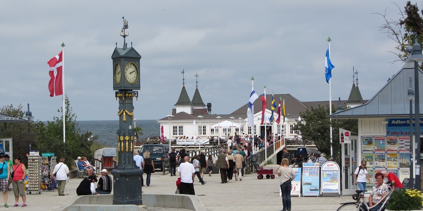 An image showing the beach promenade in Ahlbeck with a clock and a scenic pier in the distance.
