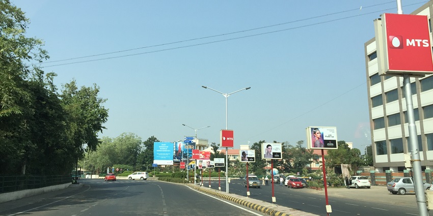 A wide, paved road curves to the right, lined with red MTS advertisement and billboards
