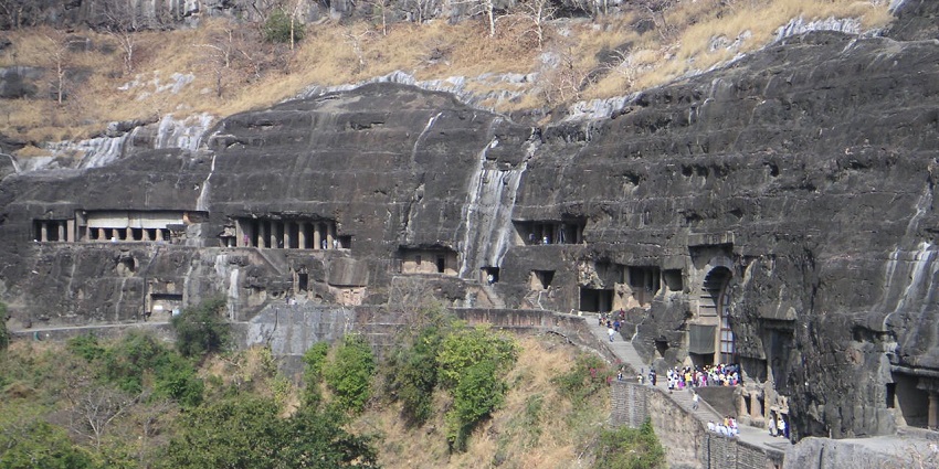 An image of ancient rock-cut Ajanta caves, with intricate carvings, surrounded by a group of visiting people