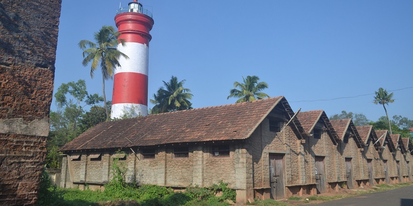 People standing and sitting at the top of the Alappuzha lighthouse painted red and white.