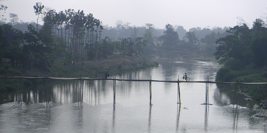 Amarsagar Lake with a small wooden bridge over the lake and two people on bicycle