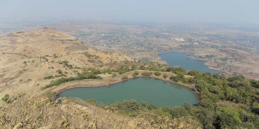 Anjaneri Lake from the top with bright blue lakes, distant buildings and a shadow on the grass.