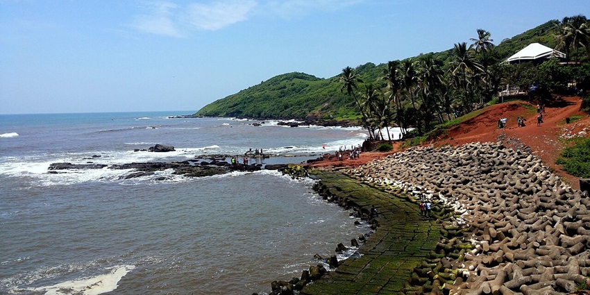 Anjuna beach with receding tide revealing wet sand and distant rocky shoreline