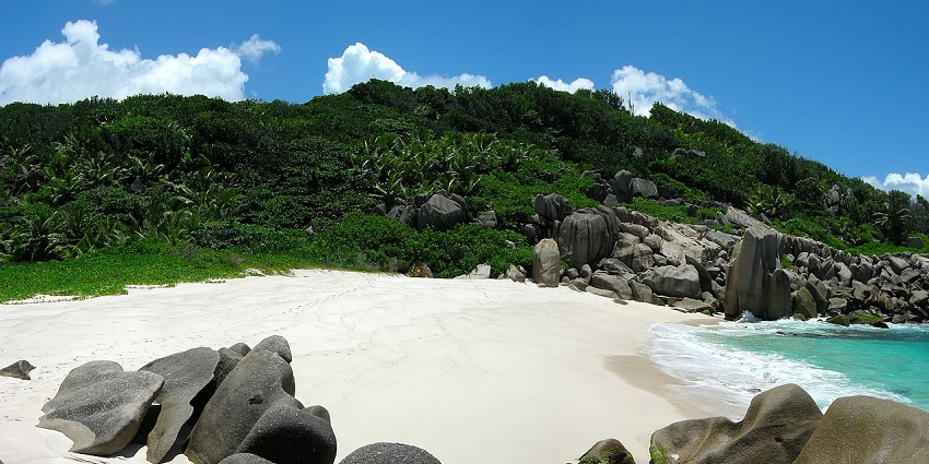 An image of a beach, covered with striking boulders and white sand under clear blue sky