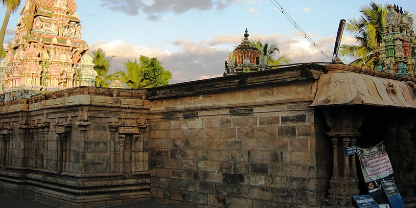 A temple structure with small, vibrant gopurams and walls made up of stone and trees