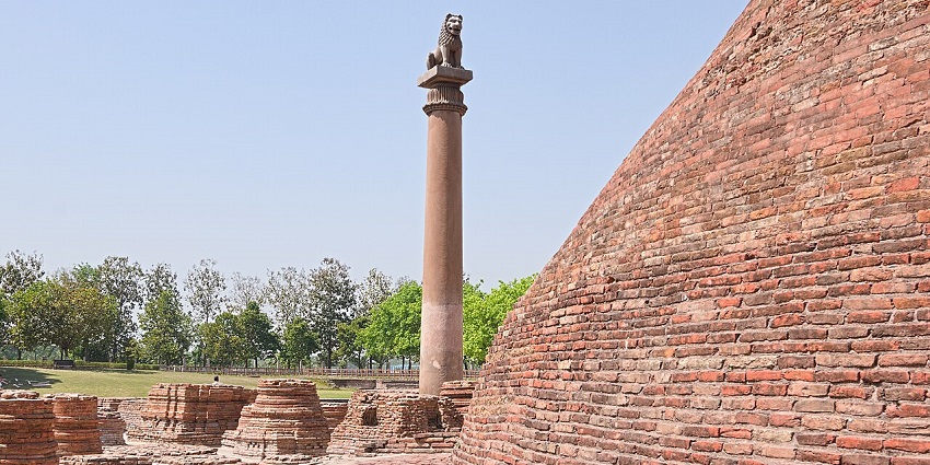 View of the Ashokan Pillar alongside a stupa in broad daylight.
