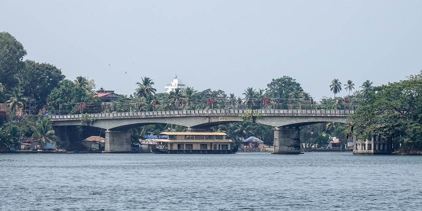 Ashtamudi Lake with a yellow houseboat passing under the bridge built on the lake.