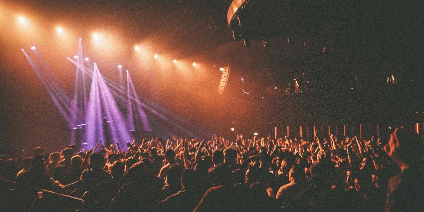 Crowded club with bright stage lights and an enthusiastic audience raising their hands.