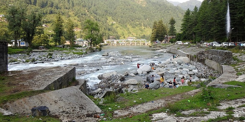 Barot valley with a small river flowing through the valley, people on the rocks and buildings.
