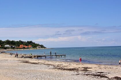 An image of a beautiful beach in Denmark with clear blue waters and sandy shores.