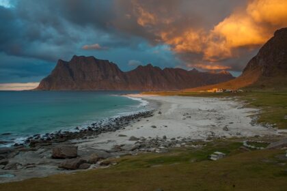 An image of a beautiful beach in Norway with clear blue waters and a backdrop of stunning mountains.