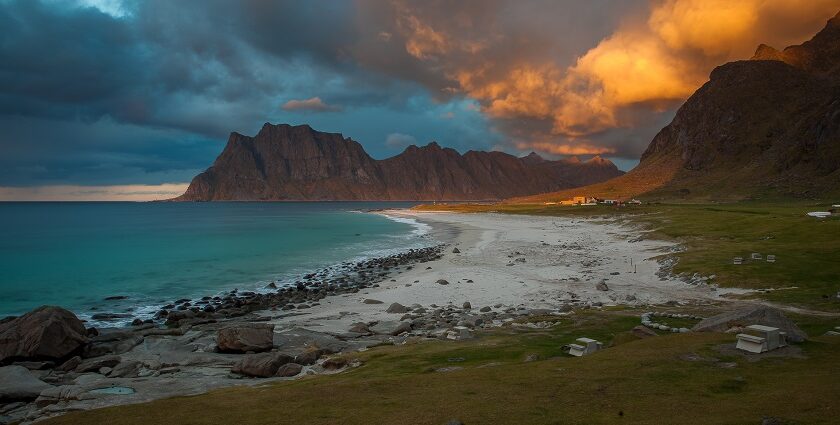 An image of a beautiful beach in Norway with clear blue waters and a backdrop of stunning mountains.