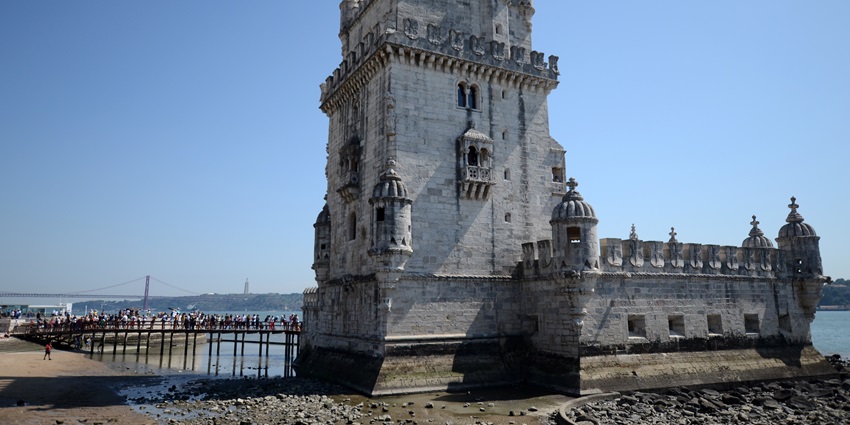 Visitors queue at a small bridge connecting Belem Tower on a sunny day in Lisbon.
