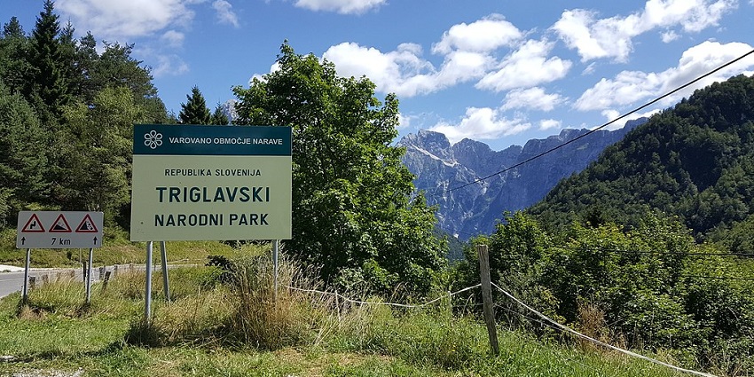 A sign for Triglav National Park in Slovenia, with mountains visible in the background