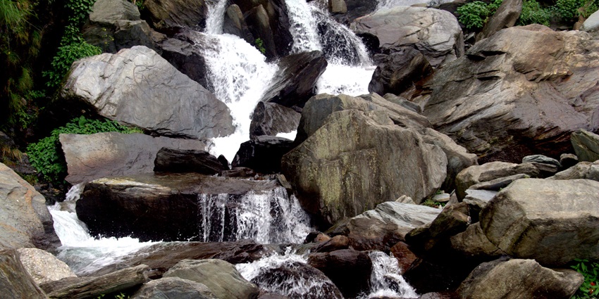 An image showing a close view of Bhagsu Waterfall with water cascading down rocky terrain.
