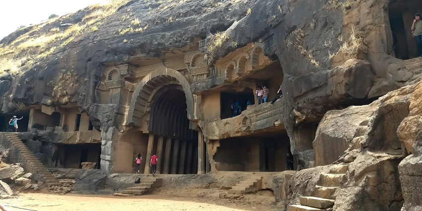  An image of a person taking a photo in front of ancient rock-cut caves on a cloudy day
