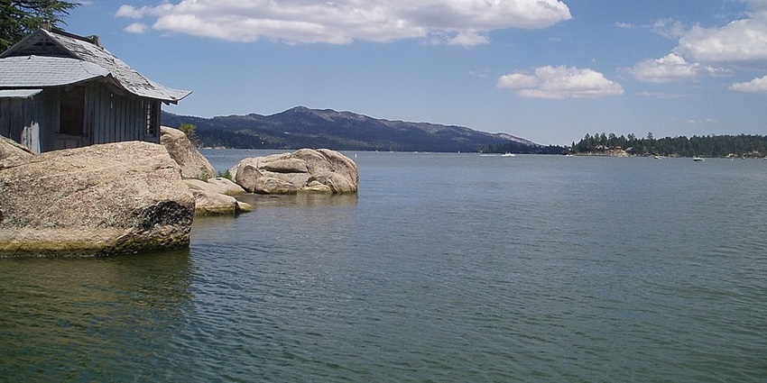 Big bear lake in California with rocks and a grey hut on the rocks under a cloudy sky