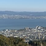 Lake Biwa from above, surrounded by the city of Shiga, tall buildings, towers and hills.