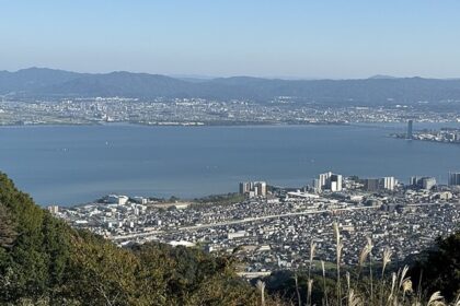 Lake Biwa from above, surrounded by the city of Shiga, tall buildings, towers and hills.