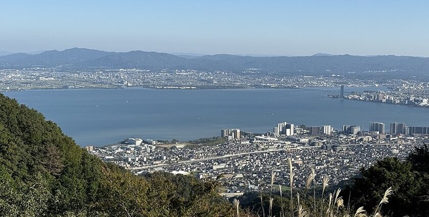 Lake Biwa from above, surrounded by the city of Shiga, tall buildings, towers and hills.