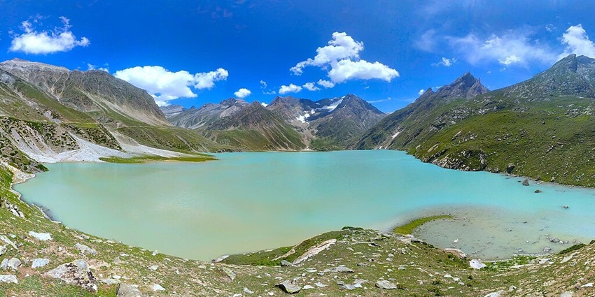 Lake with a bright cyan water body surrounded by greenery shorelines and mountains