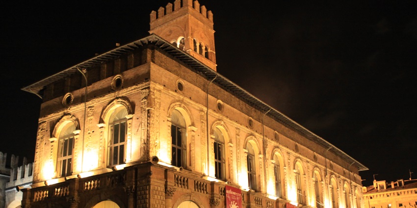 An image of Bologna's Palazzo del Podestà at night, with its illuminated facade and tower.