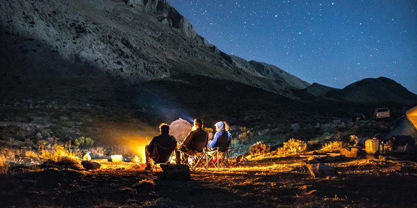 Camp near the Prashar Lake in summer near a bonfire with mountains and sky covered in stars.
