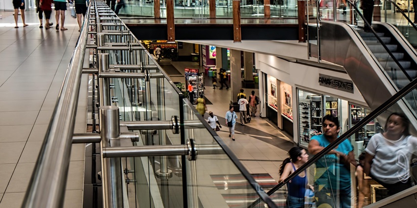 An image of a busy shopping mall with people walking on escalators and exploring the stores.