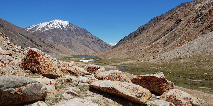 Chagar Tso with a small water body, big rocks and a mountain partially covered in snow