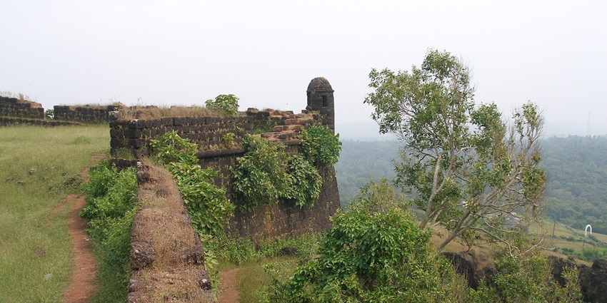 An image of the Chapora fort, with an old stone fort wall with greenery and a scenic view