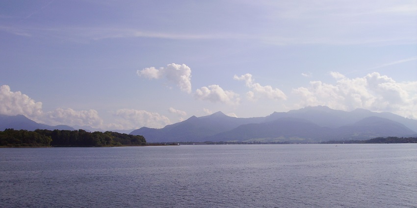 Chiemsee Lake with a large water body and mountains in the background under the cloudy sky