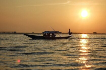 Silhouette of a boat with people in it and reflection of sunsetting on the Chilika Lake