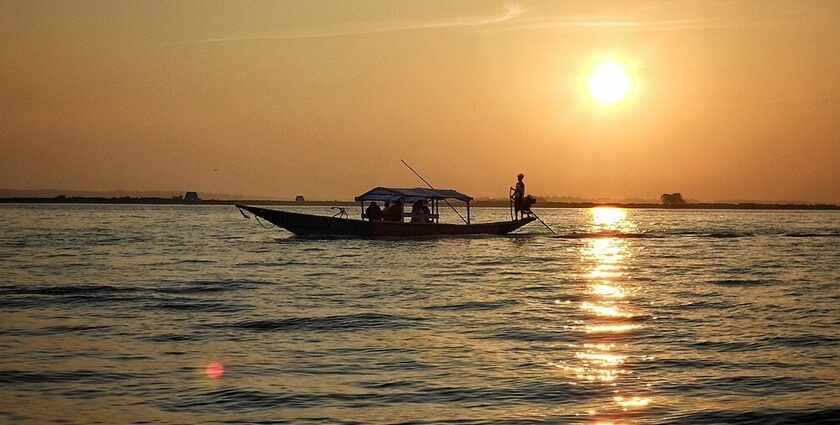 Silhouette of a boat with people in it and reflection of sunsetting on the Chilika Lake