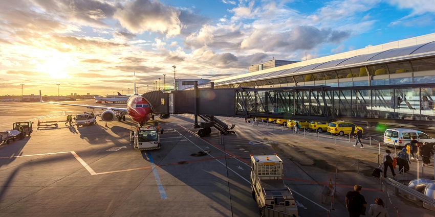 A plane parked at an airport gate, with a jet bridge connected and ground crew working around the aircraft.