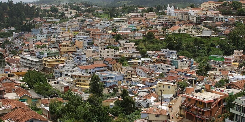 An image showing the town of Coonoor as seen from a hillside, with buildings and greenery.