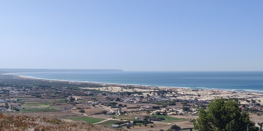 A vast expanse of blue ocean meeting a long, sandy beach bordering a town with buildings
