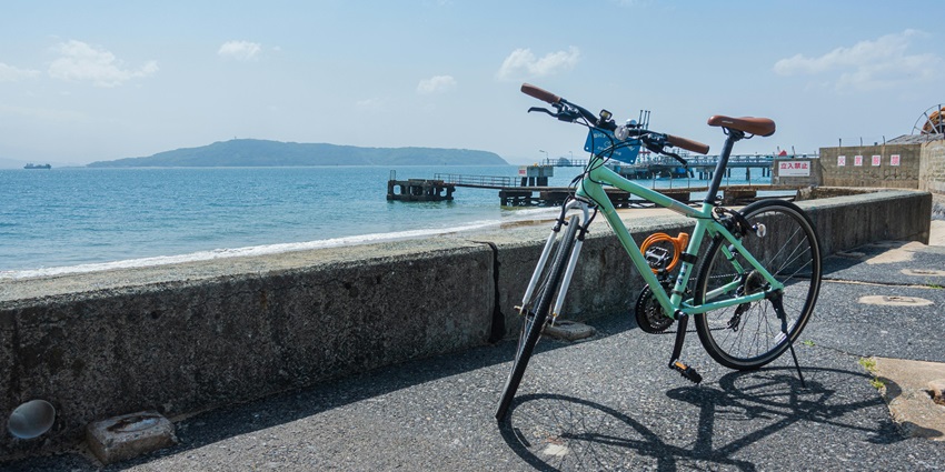Cyan-coloured bicycle parked on a road next to a vast lake and distant hills beyond it.