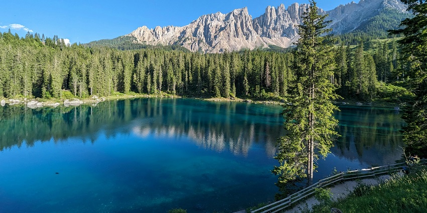 A clear lake surrounded by tall green trees with rocky mountains in the background