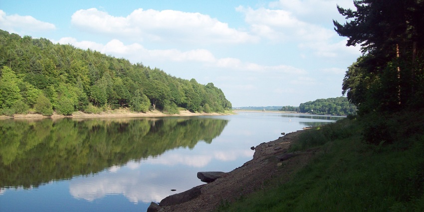 Damflask Reservoir in Loxley valley showing blue waters, clear skies, a boat and hills around