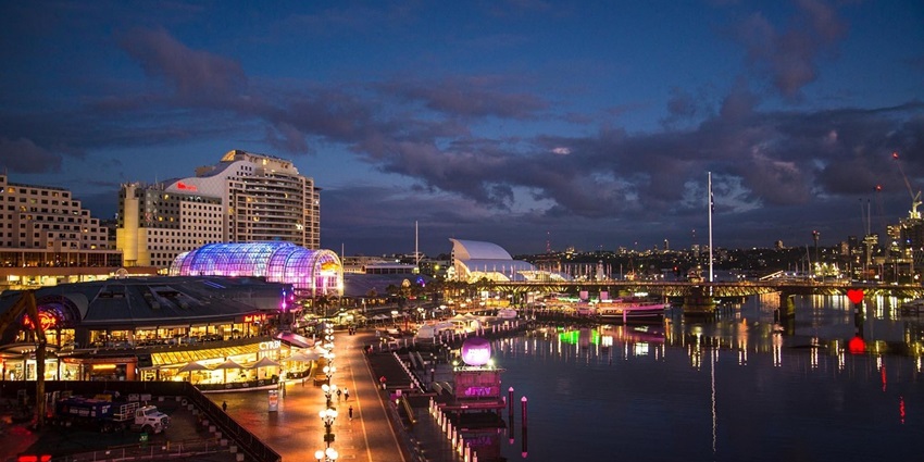 An evening view of Darling Harbour in Sydney, showcasing colorful lights and lively waters