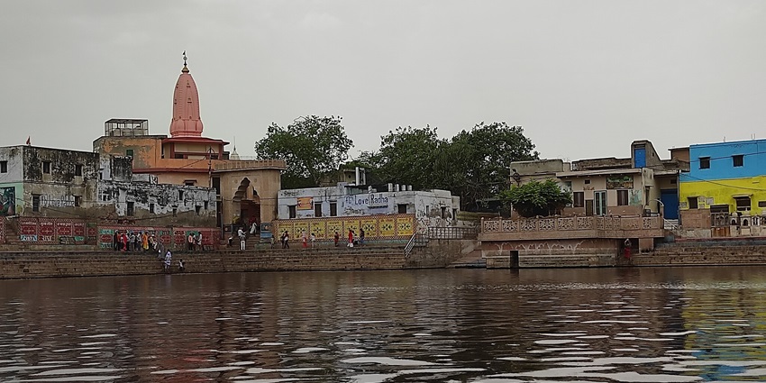 Radha Kund with people standing on the stairs and temples and buildings in the back