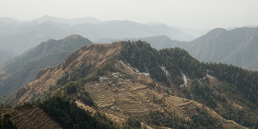 View of layered mountain ranges with terraced fields and evergreen forests of Dhanaulti