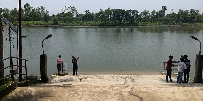 A man takes a photograph from his phone while standing near a lake on a sunny day