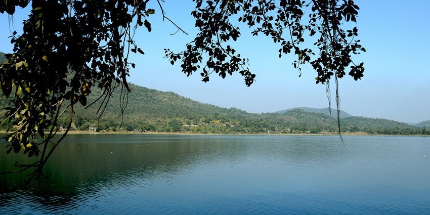 Dimna Lake offers a breathtaking panorama with lush green mountains beneath a clear sky.