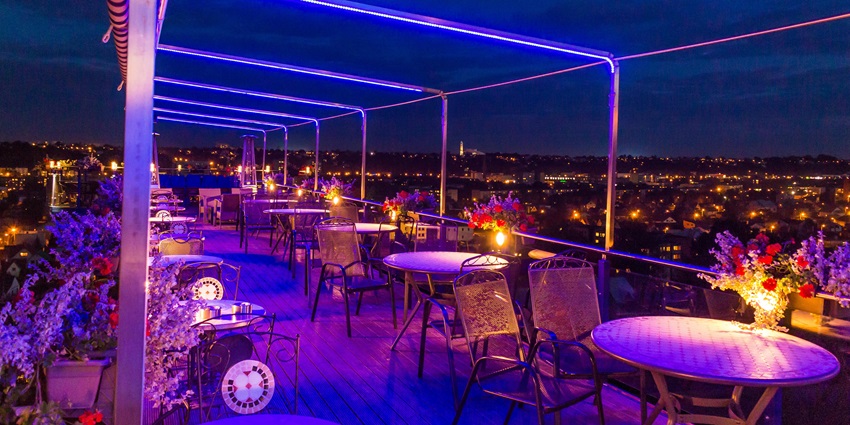 A rooftop café with fairy lights, cozy seating, and a view of the Salt Lake skyline at dusk.
