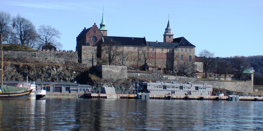 An image of Akershus Fortress in Oslo, Norway, viewed from the water with boats docked nearby.