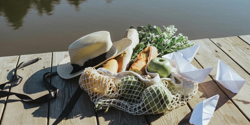Image of Paper Boats Lying Next to Bag of Food and Straw Hat on Pier on the deck of a lake