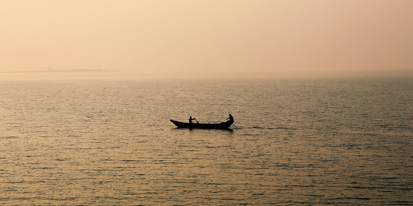 A picture of a man riding a boat in the largest artificial lake in India.