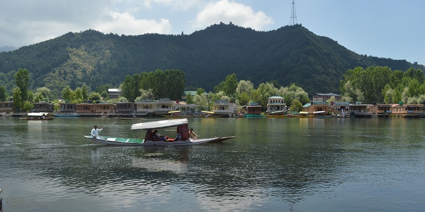 People on a shikhara ride on the Manasbal Lake in Kashmir with several boats parked near the shore.