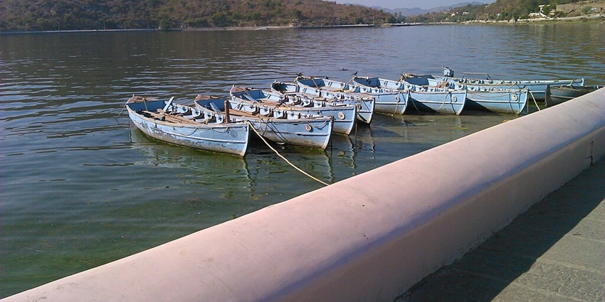 A picturesque scene of Fateh Sagar Lake on a sunny day with boats and distant mountains
